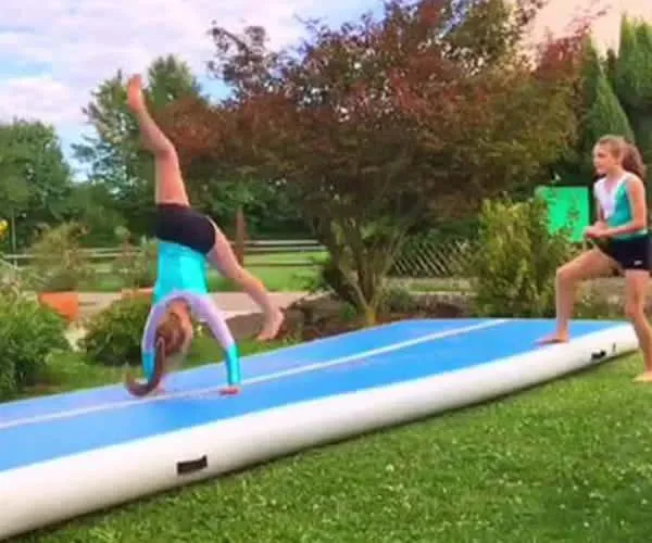 Two women doing gymnastics on an inflatable mat made of drop stitch fabric on a green grass